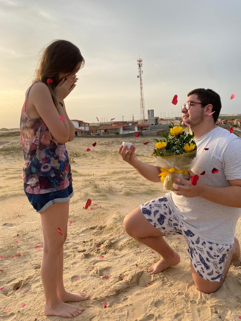 Adrison ajoelhado fazendo o pedido de casamento a Vitória, entre pétalas